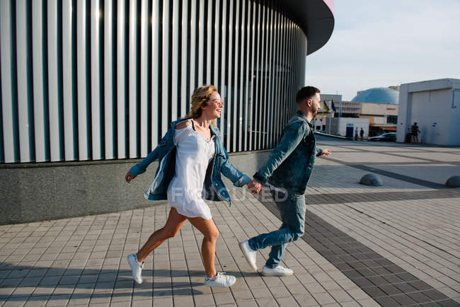 Vista lateral de correr joven pareja adulta en ropa casual - foto de stock