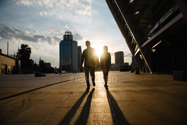 Vue panoramique des silhouettes de couple de jeunes adultes contre la lumière du coucher du soleil — Photo de stock