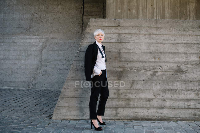 Жінка в класичному костюмі позує на бетонну стіну — стокове фото