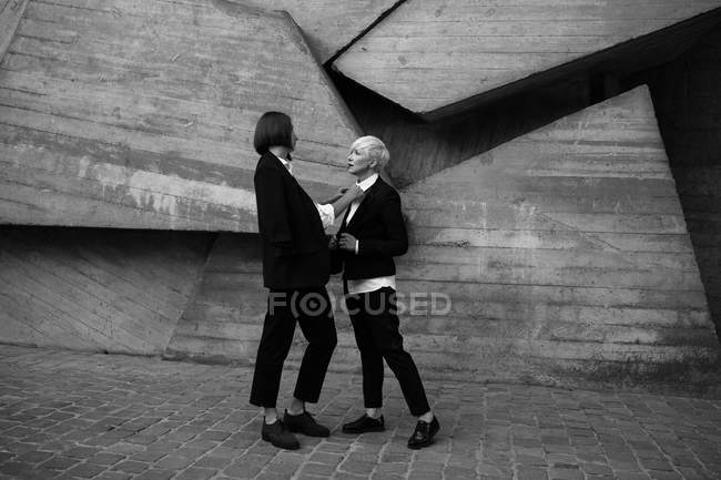 Full length colpo di donna legare legare legare il suo amico contro muro di cemento geometrico all'aperto — Foto stock