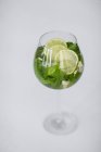 Primo piano vista della bevanda ghiacciata con foglie di menta e fette di lime in vetro su superficie bianca — Foto stock