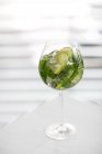 Vue rapprochée de la boisson glacée avec des feuilles de menthe et des tranches de citron vert en verre sur surface blanche — Photo de stock