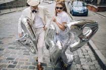 Stilvolles Paar spaziert mit silbernen Luftballons auf der Stadtstraße — Stockfoto