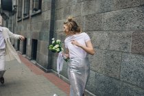 Newlywed man chasing laughing bride on city street — Stock Photo