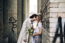 Couple nouvellement marié appuyé sur le mur de bord et riant — Photo de stock