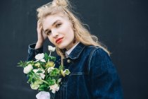 Portrait of young blonde woman in denim jacket holding bouquet — Stock Photo