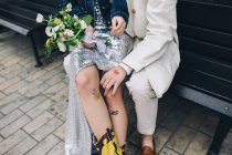 Femme nouvellement mariée assise sur le genou du marié sur un banc urbain — Photo de stock