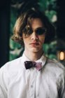 Portrait of young man with curly hair in sunglasses and bow tie — Stock Photo