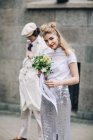 Beautiful newlywed woman with bridal bouquet and groom in background — Stock Photo