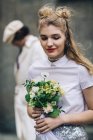 Beautiful newlywed woman with bridal bouquet and groom in background — Stock Photo