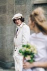 Serious newlywed man in newsboy cap with bride in foreground — Stock Photo