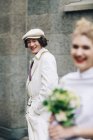Newlywed man in newsboy cap smiling with bride in foreground — Stock Photo