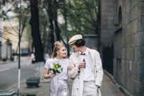 Newlywed couple walking hand in hand on city street — Stock Photo