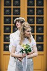 Casal recém-casado abraçando posando com buquê de noiva contra a porta do prédio — Fotografia de Stock
