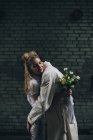 Щаслива наречена обіймає нареченого з весільним букетом на вулиці міста — стокове фото