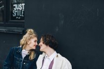 Young couple sitting face to face in front grunge building wall — Stock Photo