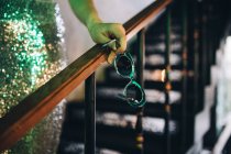 Cropped view of female hand holding sunglasses and leaning on banister — Stock Photo