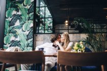 Fashionable newlywed couple kissing in cafe interior — Stock Photo