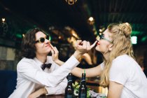 Young couple in sunglasses touching faces and having fun in bar interior — Stock Photo