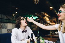Young couple in sunglasses touching faces and having fun in bar interior — Stock Photo