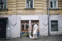 Newlywed woman sitting on bicycle decoration with man in city — Stock Photo