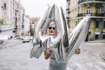 Stylish woman posing with silver balloons on city street — Stock Photo