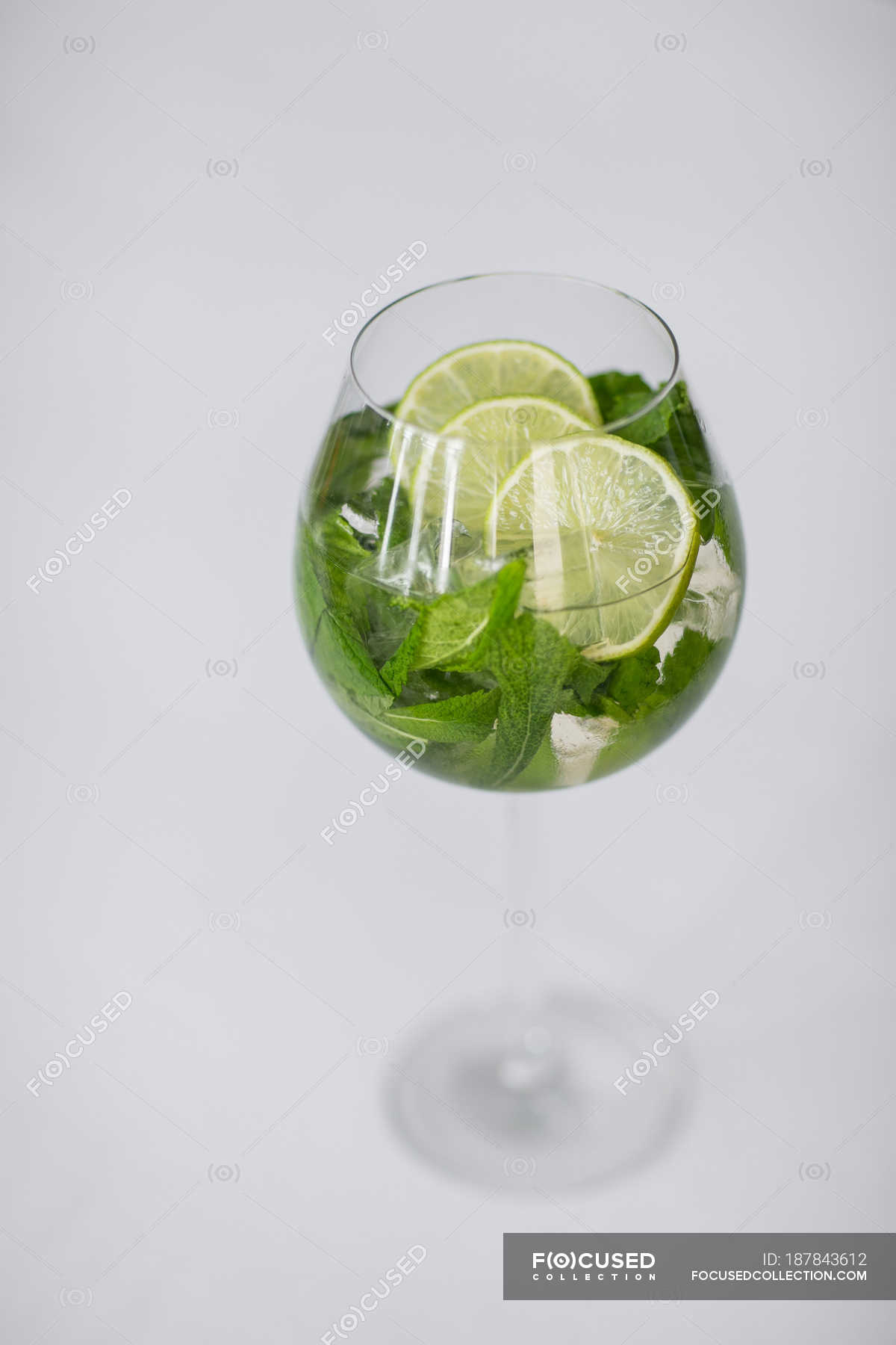 Closeup view of iced drink with mint leaves and lime slices in glass on white surface — organic