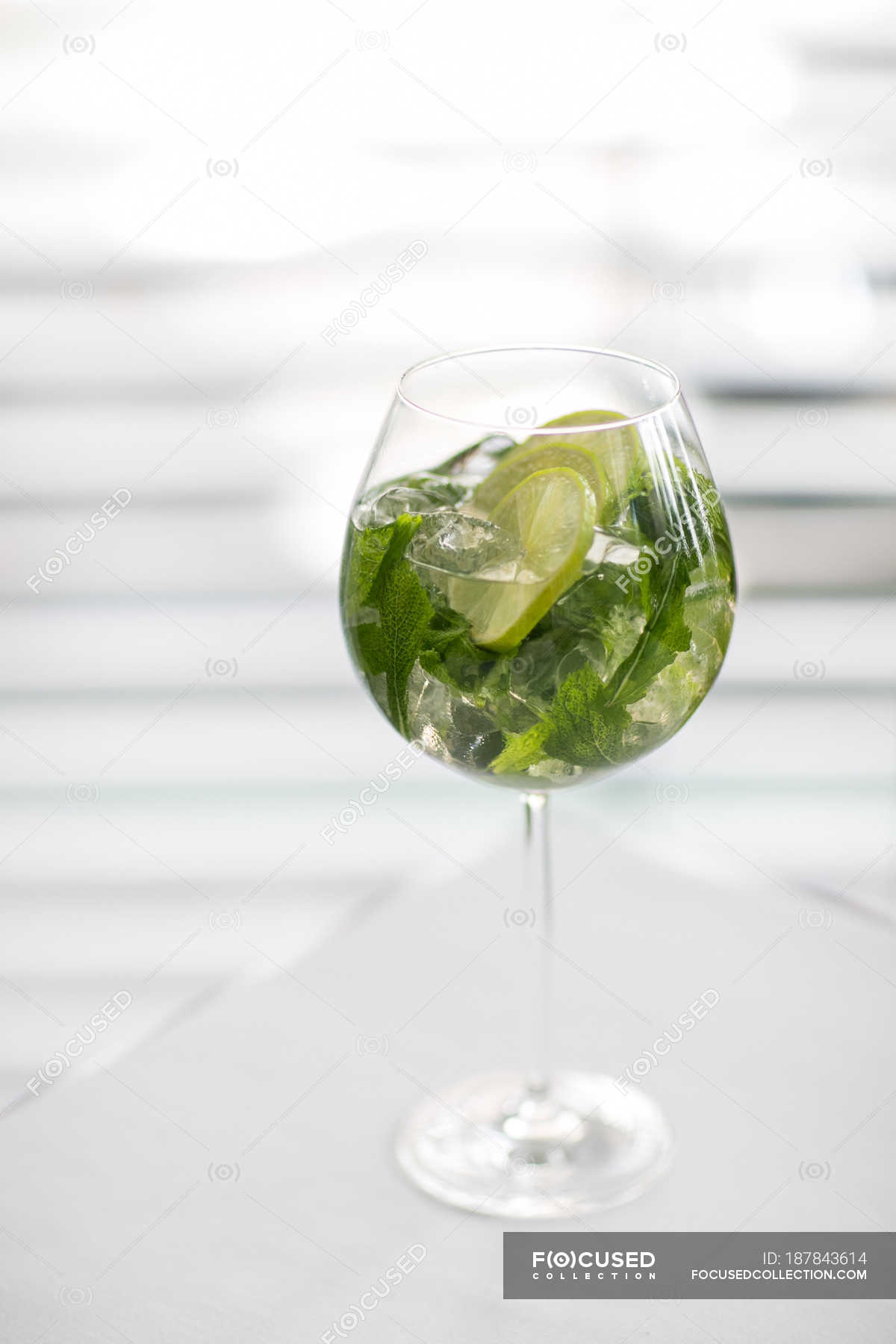 Closeup view of iced drink with mint leaves and lime slices in glass on white surface — edible