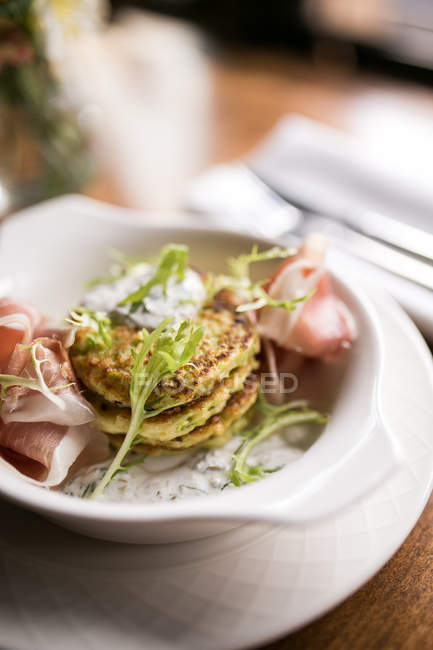 Closeup view of potato flapjacks with ham, sauce and herbs in bowl — Stock Photo