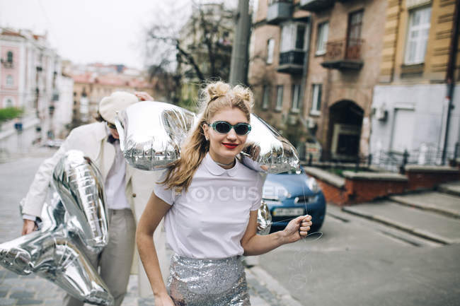 Casal elegante andando com balões de prata na rua da cidade — Fotografia de Stock