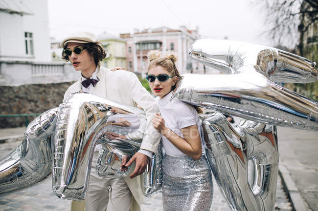 Stilvolles Paar spaziert mit silbernen Luftballons auf der Stadtstraße — Stockfoto