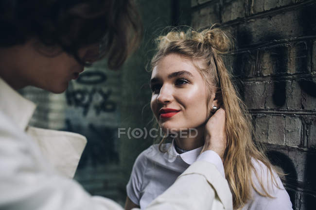 Jovem tocando rosto feminino contra parede de tijolo urbano — Fotografia de Stock