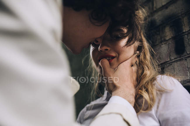 Young man touching female lips against urban brick wall — Stock Photo