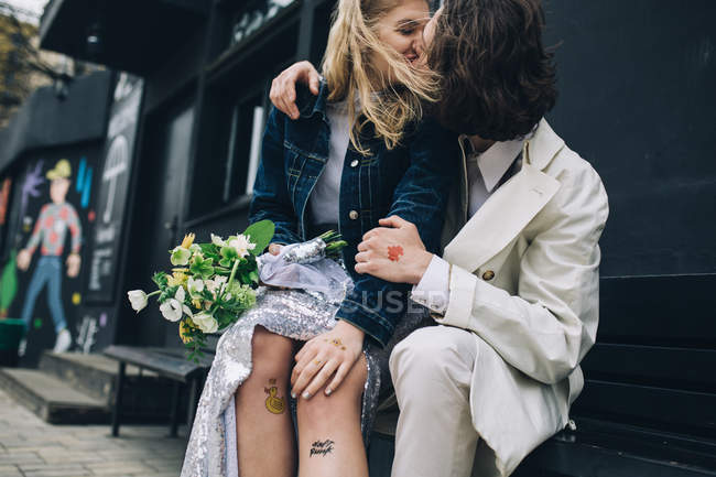 Recién casada pareja besándose en ciudad urbana banco - foto de stock