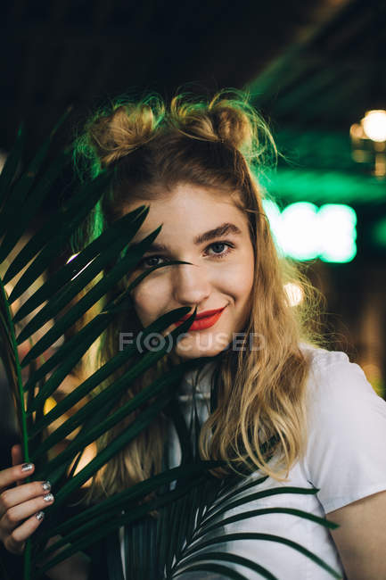Portrait of young woman with double-bun hairstyle hiding behind plant — Stock Photo