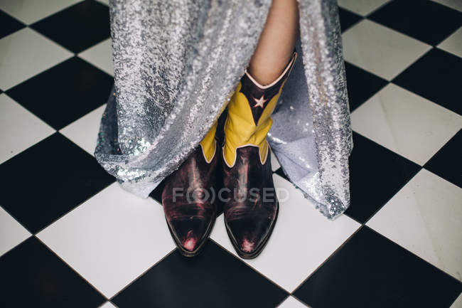 Обрезанный вид женских ног с длинной серебряной юбкой и ковбойскими сапогами — стоковое фото