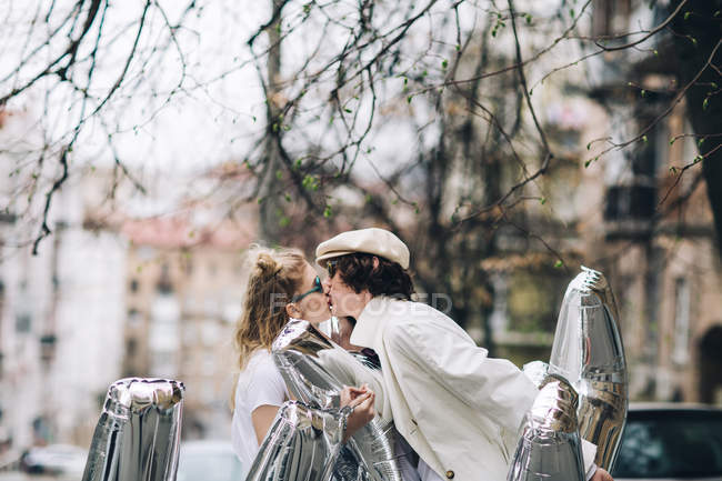 Pareja de moda besándose con globos de plata en la calle - foto de stock