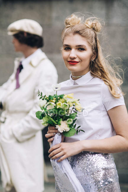 Красива молода жінка з весільним букетом і нареченим на задньому плані — стокове фото