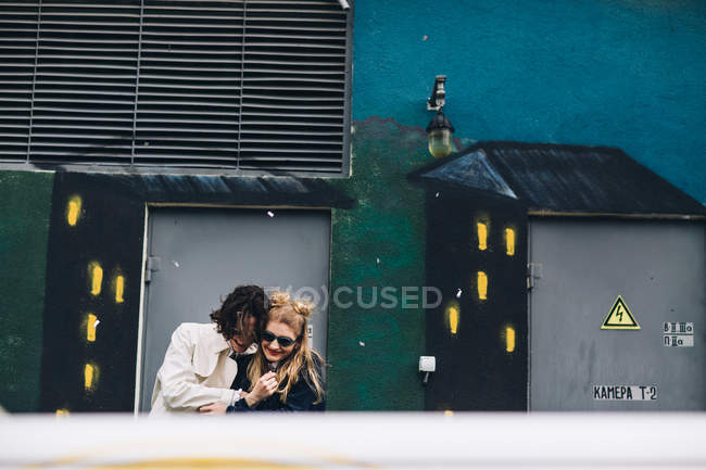 Cena urbana de casal abraçando e rindo contra a parede pintada — Fotografia de Stock