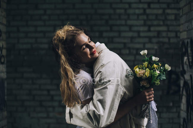 Glückliche Braut umarmt Bräutigam mit Brautstrauß in urbaner Backstreet — Stockfoto