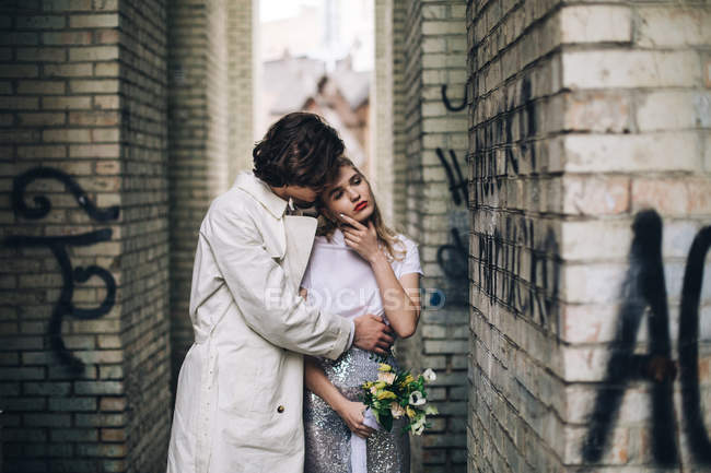Urban scene of newlywed couple hugging in front of brink wall — Stock Photo