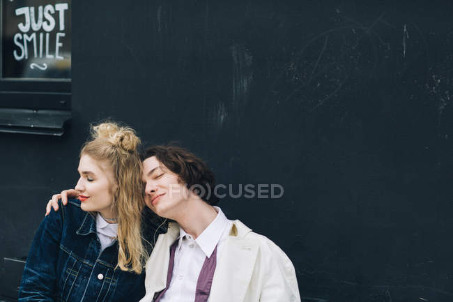 Young man leaning on girlfriend shoulder in front grunge building wall — Stock Photo