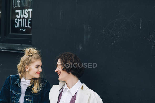 Jeune couple assis face à face devant le mur de bâtiment grunge — Photo de stock
