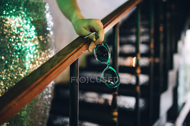 Cropped view of female hand holding sunglasses and leaning on banister — Stock Photo