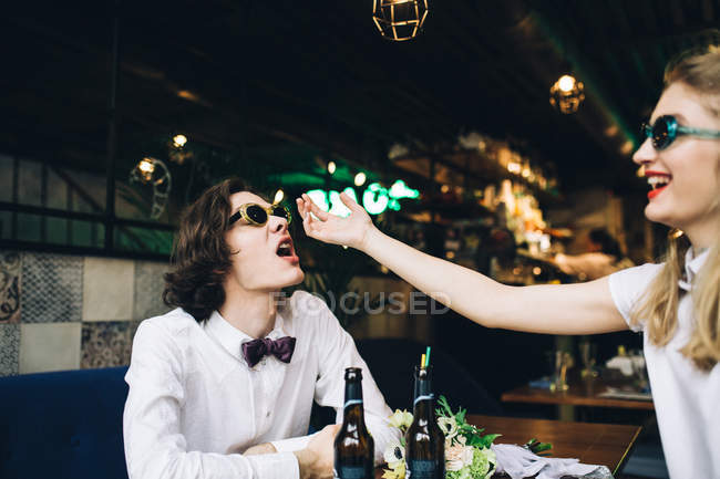 Junges Paar mit Sonnenbrille berührt Gesichter und hat Spaß in Bar-Interieur — Stockfoto
