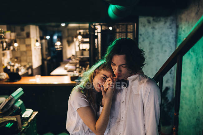 Молодой человек держит и целует подружку рука об руку в баре — стоковое фото