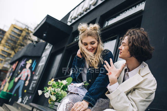 Elegante pareja de recién casados sentados en el banco de la ciudad - foto de stock