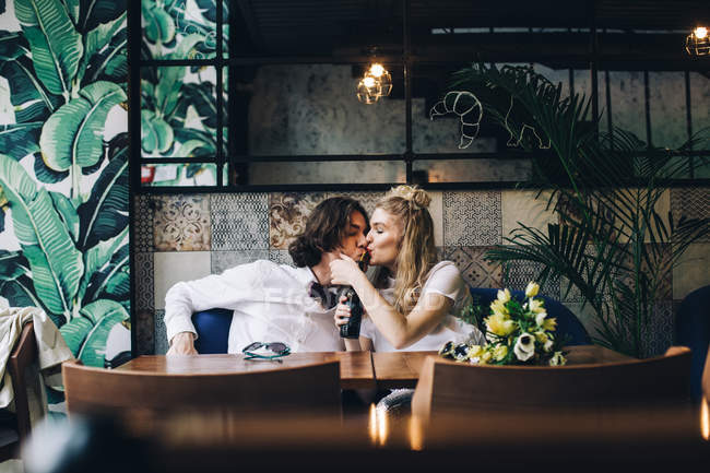 Junge Frau küsst Mann, während sie aus Flasche im Café trinkt — Stockfoto