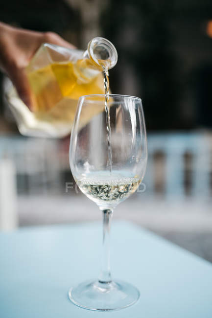 Abgeschnittenes Bild einer männlichen Hand, die Weißwein ins Weinglas gießt — Stockfoto