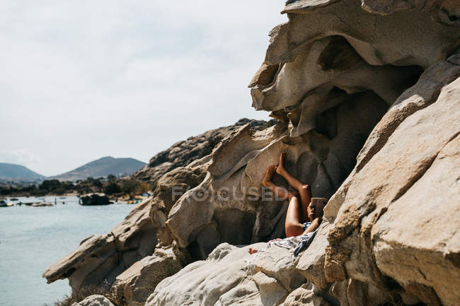 Femme couchée sur la plage volcanique et livre de lecture, Paros, Mer Égée, Cyclades, Grèce — Photo de stock